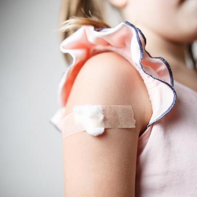 Close up of child's upper arm with a cotton ball and tape covering vaccination site. 