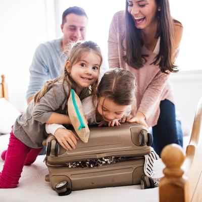 A happy family trying to close a packed suitcase.