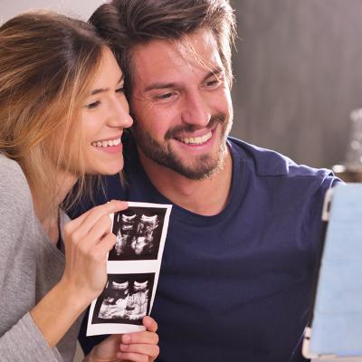 A young couple sharing ultrasound photographs while in a virtual call with loved ones.