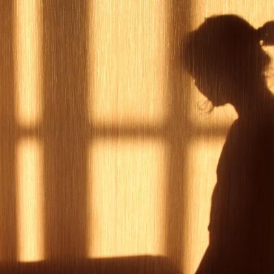 Silhouette of a person with a short ponytail and crossbars of a window on the against a wooden wall. 