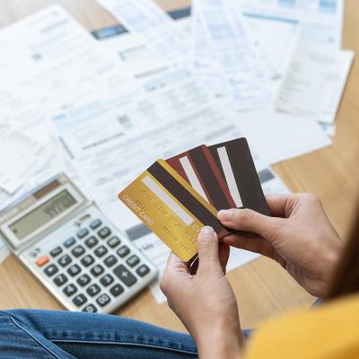 Young woman holding several credit cards and calculating a pile of bills.
