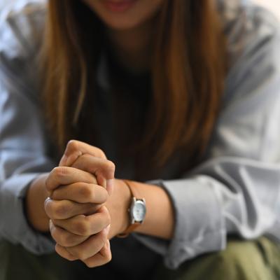 Sad woman sitting on a sofa with hands clasped.