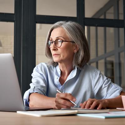Senior woman looking up information online and writing notes.