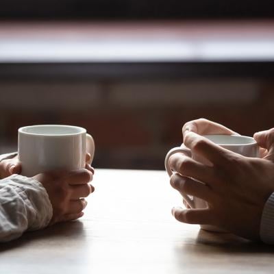 A Gen Z and Millenial sitting across each other at a table drinking coffee.