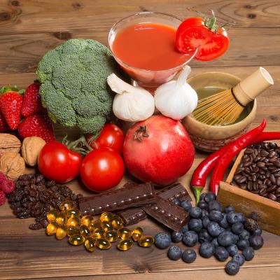 Healthy antioxidants foods like broccoli, berries, tomoatoes, pomegranates, green tea, coffee, nuts and chocolate  on a wooden table.