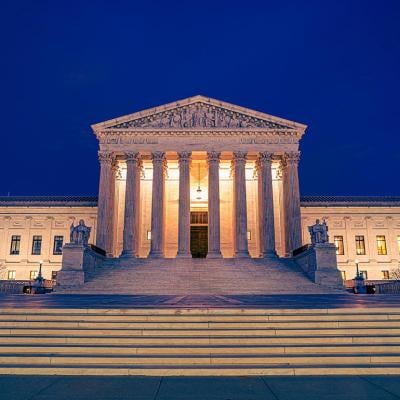 United States Supreme Courts building illuminated at night in Washington DC with steps and plaza in foreground.