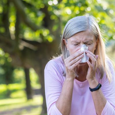 Senior woman outdoors wiping her nose with a napkin.