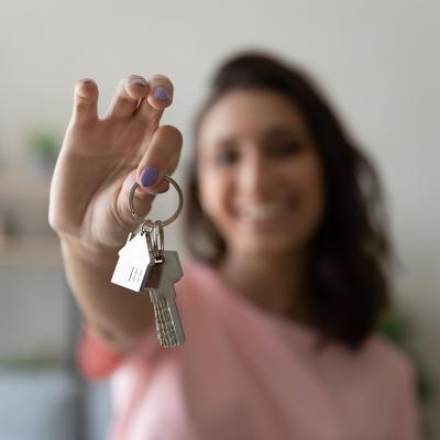 A young female homeowner holding up the keys to her house.
