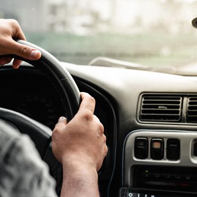 Close-up of a man holding the steering wheel while driving on the road.
