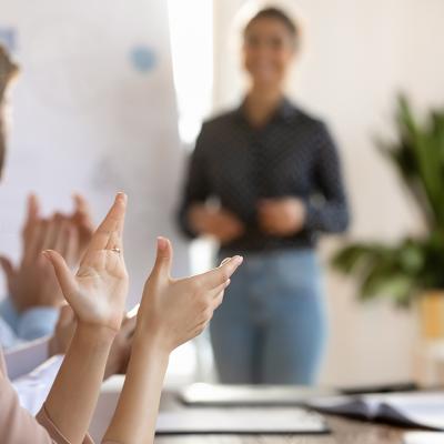 Members of a team applaud another member after a successful meeting presentation.