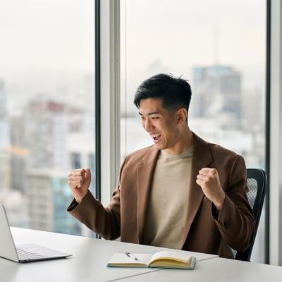 Businessman celebrating a success at work in front of a laptop.