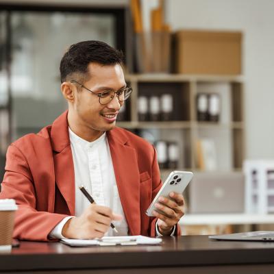 Small business owner holding a phone on his one hand and writing down information with the other.