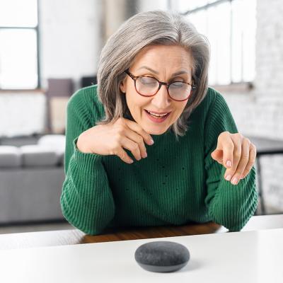 Retired woman using a voice command on a smart speaker with AI at home.