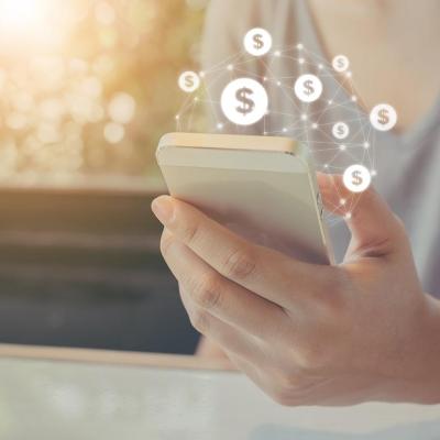 Hand holding mobile phone with dollar sign icons overlaid, symbolizing ecommerce transactions made on smartphones.