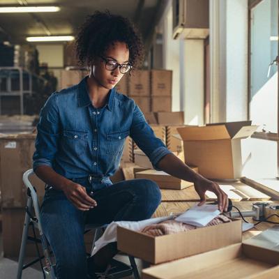Black woman wearing denim outfit prepares packages for shipping in a fulfillment office.