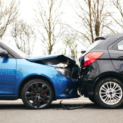 Two cars involved in traffic accident on side of the road with damage to hood and fender.