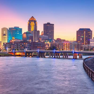 Cityscape image of Des Moines skyline, Iowa bridge over water with summer sunset.