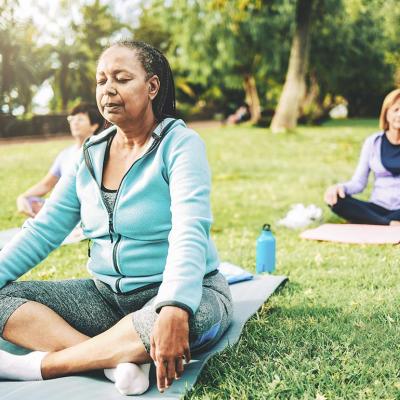 Three people in seated yoga poses on individual yoga mats on a green lawn, not sitting close together.