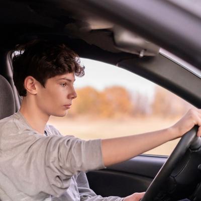 Young male driver holding steering wheel in car seen through the passenger side window.