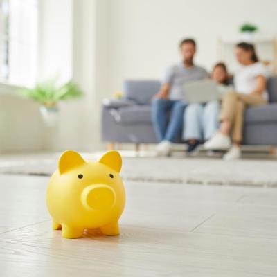 Yellow piggy money box standing on floor in the living room and a parents with a child girl sitting on sofa at home in background.