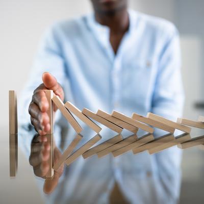 A businessman stopping a row of domino wooden bricks with his hand.