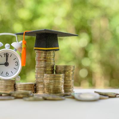 A clock and graduation cap on top of coins as a concept of student loans.