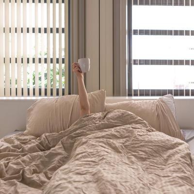 Hand holding a coffee cup extending upward from person whose face and body are under the covers in bed.