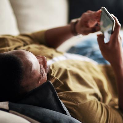Young man relaxing on a couch at home while scrolling through social media on his phone.