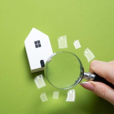 A magnifying glass looking over a figure of a house on a green background.