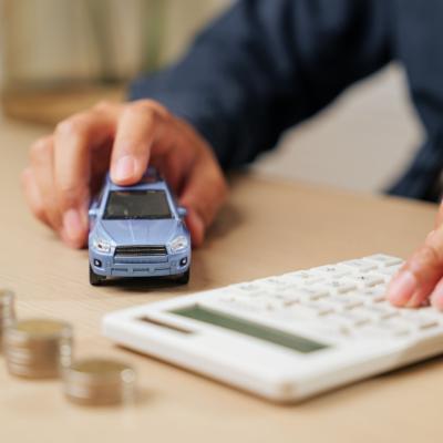 Calculator in hand as a person calculates car loan payments by a small car model and coins. 