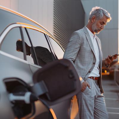 A man leaning on his electric car while using his smartphone.