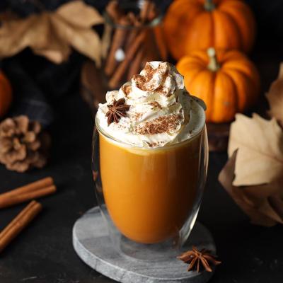 Glass of pumpkin spice latte with whipped cream and ingredients like cinnamon sticks and fall decor on black table.