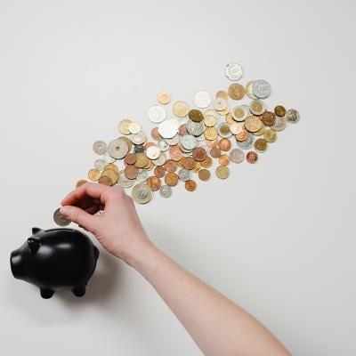 Coins being inserted into a black piggy bank.