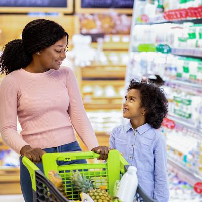 A young black mom and her daughter shopping together for groceries in a supermarket.