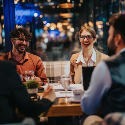 A group of business people laughing and discussing during a meeting in a modern restaurant setting. 