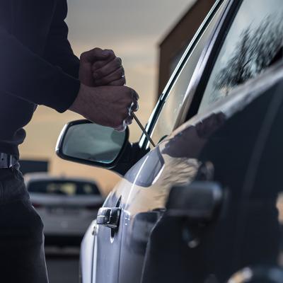 A thief trying to break into a car window with a screwdriver.