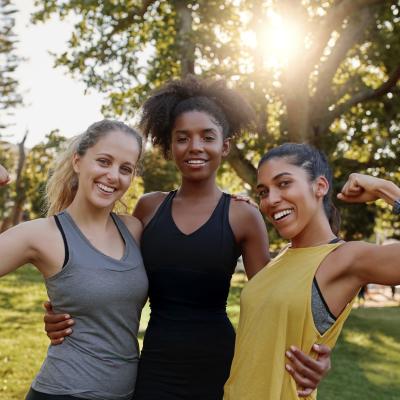 Three women flexing their muscles in a park.