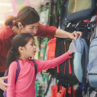 A mother helps her young daughter to pick a new bag for school at a store.