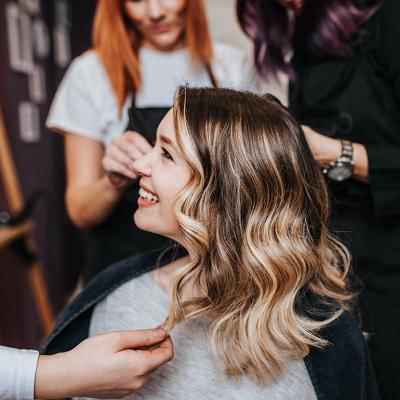 Side profile of woman with blond and brunette hair in long layers smiling at hair salon with two stylists behind her in the background.