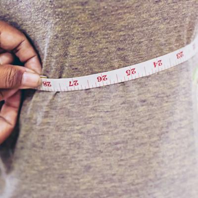 A tailor taking measurements of a client's torso with a tape measure.