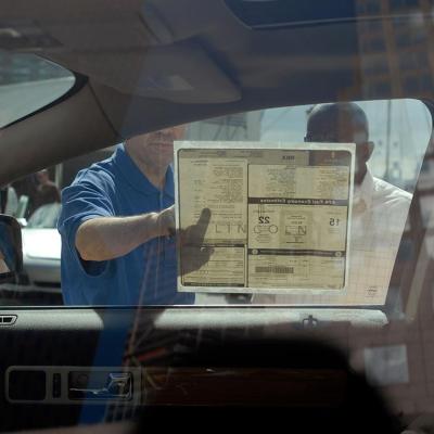 Interior view of car from driver's side looking out passenger window where two people are reading a sticker on the window with the car's features. 