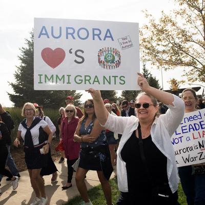People in Denver protesting the federal government's stance on immigration; one holds a white posterboard that reads "Aurora loves immigrants"