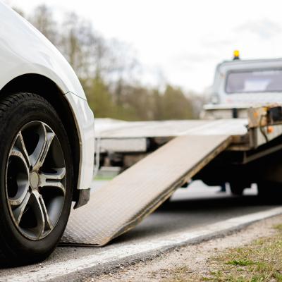 A broken car being loaded on a tow truck on roadside.