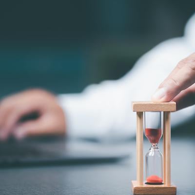 A business employee using a small time hourglass beside a laptop.