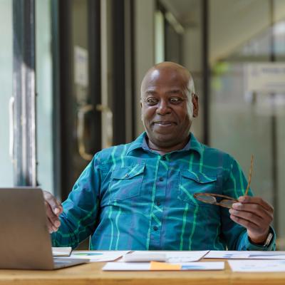 A senior man excitingly looks at financial documents while using a laptop.