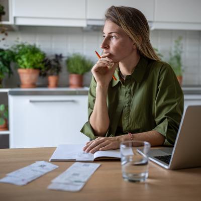 A pensive woman at home working on accounting documents.