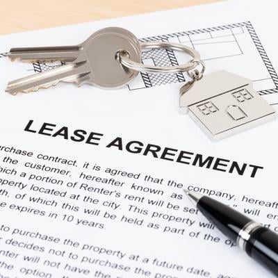 A mock up of a lease agreement document with house keys on top of it.
