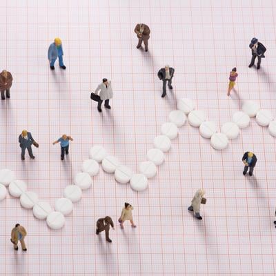 White pills forming a jagged line, dividing small figures of different people to represent different healthcare costs among groups.