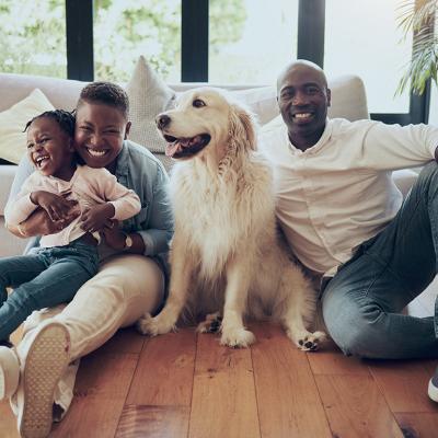 A black family of three and their dog, happily sitting on the living room floor of their home.