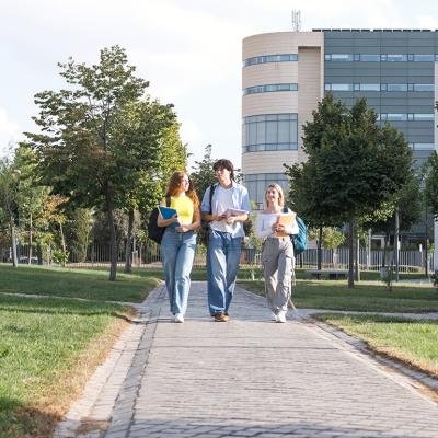 A group of three young college students chatting while walking on university campus footpath.